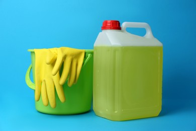 Photo of Green bucket with gloves and canister of detergent on light blue background. Cleaning supplies