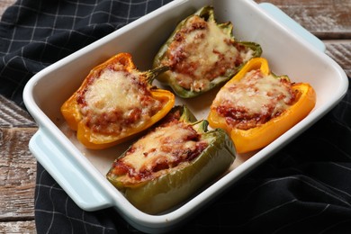 Photo of Tasty stuffed peppers in dish on wooden table, closeup