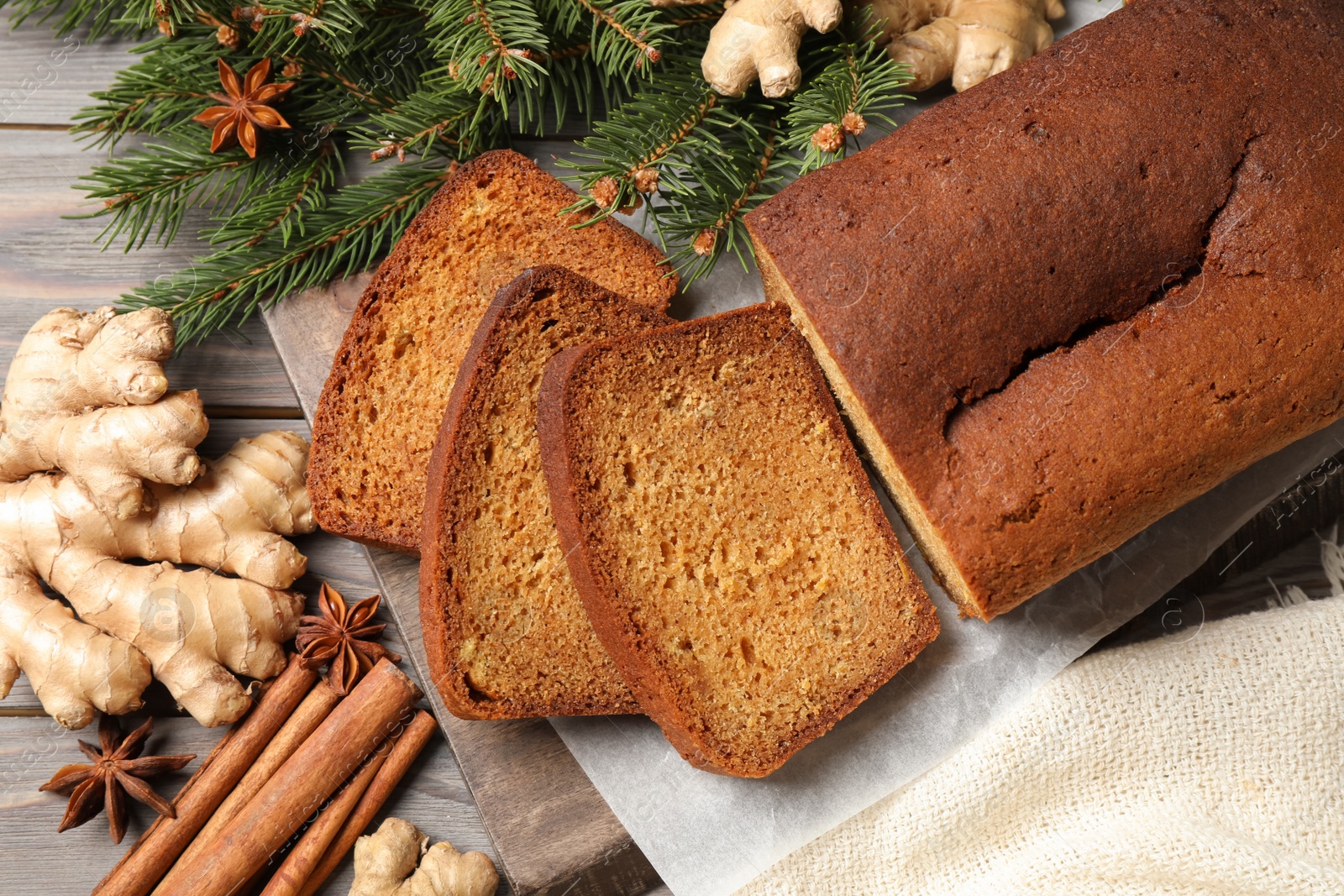 Photo of Delicious gingerbread cake, ingredients and fir branches on wooden table, flat lay