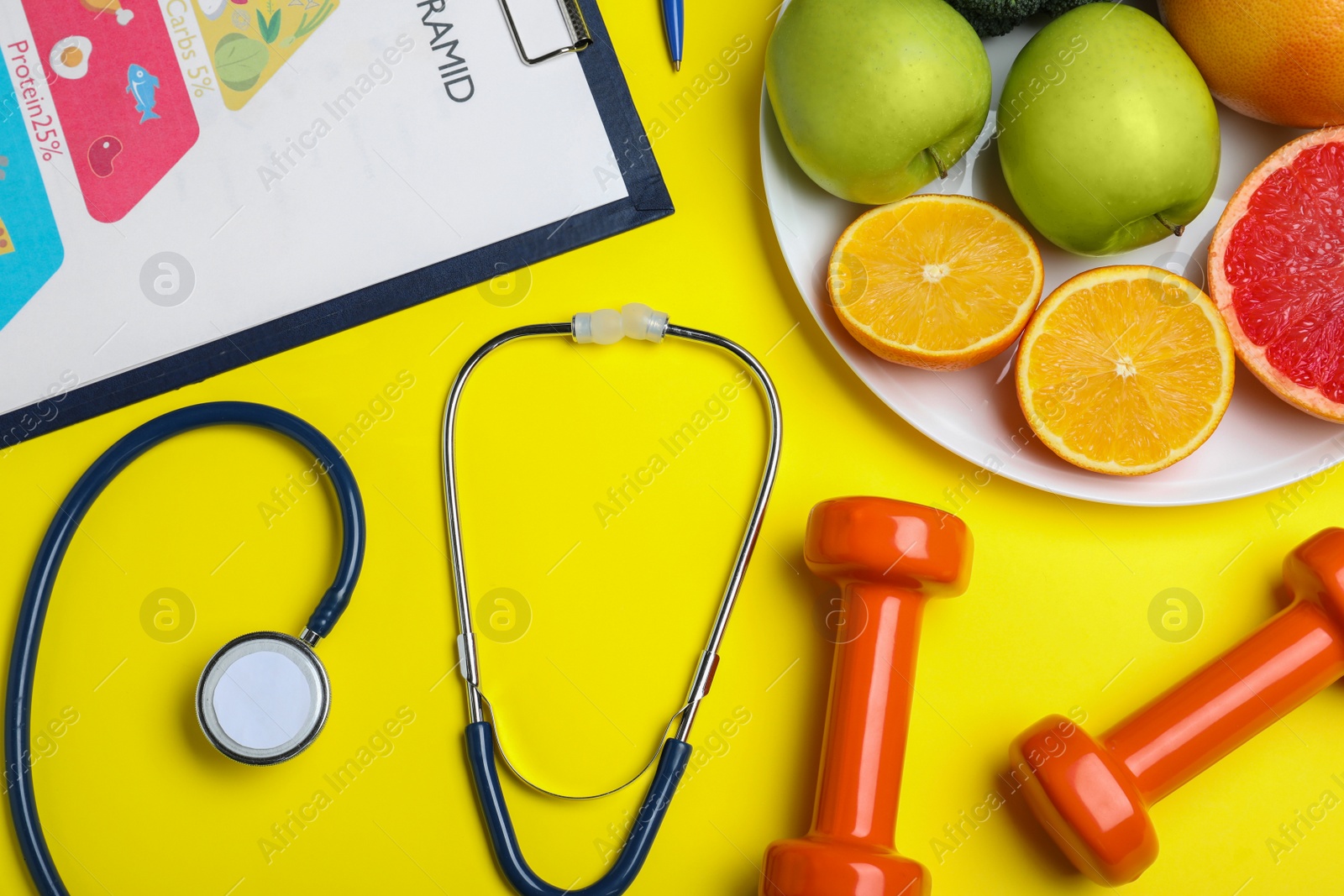 Photo of Fruits, dumbbells, stethoscope and list of products on yellow background, flat lay. Visiting nutritionist
