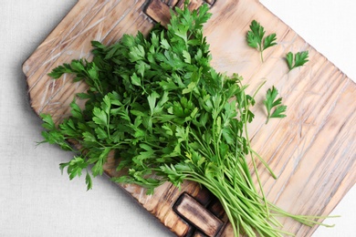 Wooden board with fresh green parsley on light fabric, top view