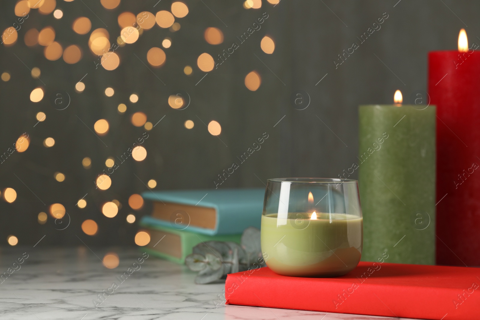 Photo of Burning candles and books on white marble table against blurred lights, space for text