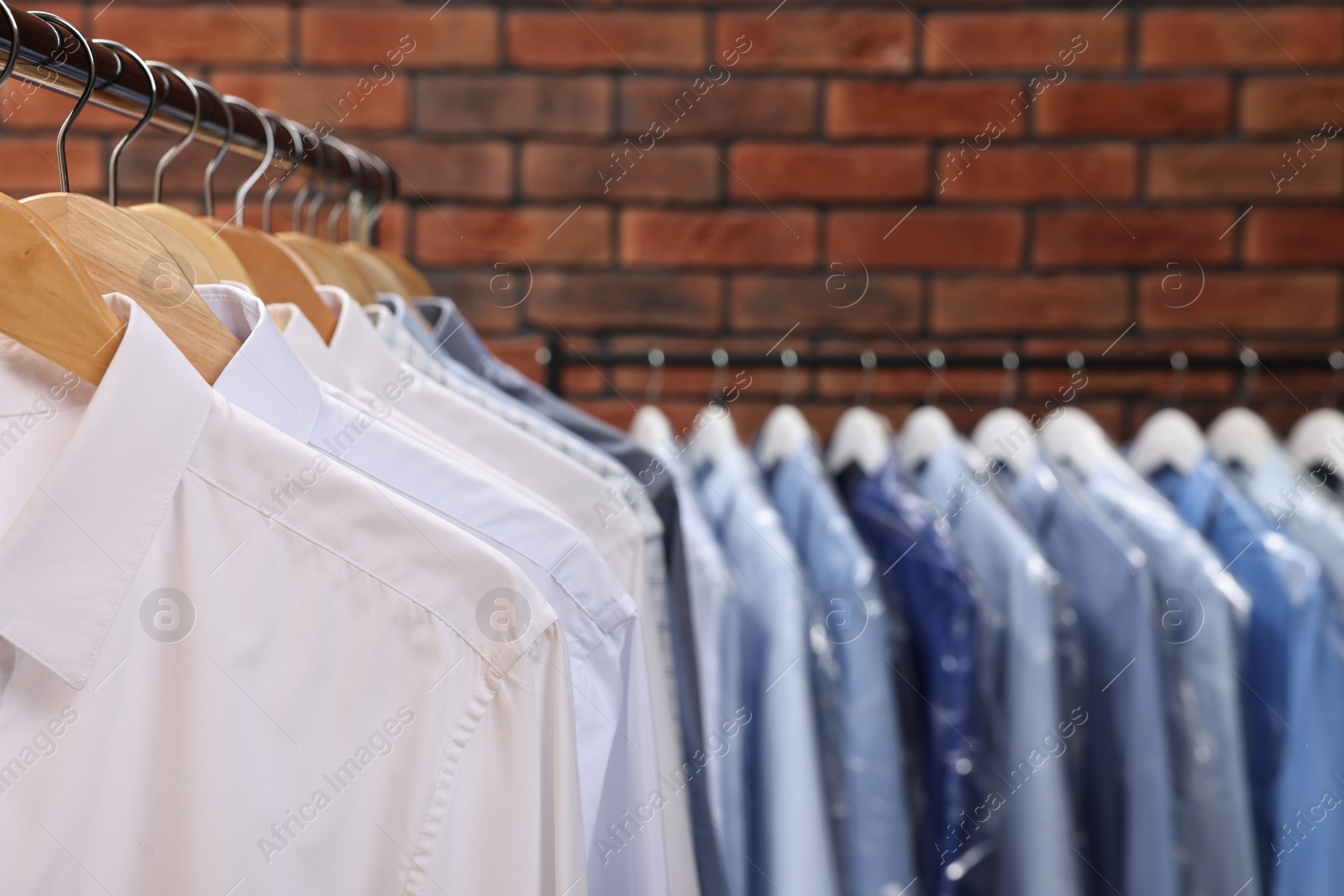 Photo of Dry-cleaning service. Many different clothes hanging on rack against brick wall, closeup