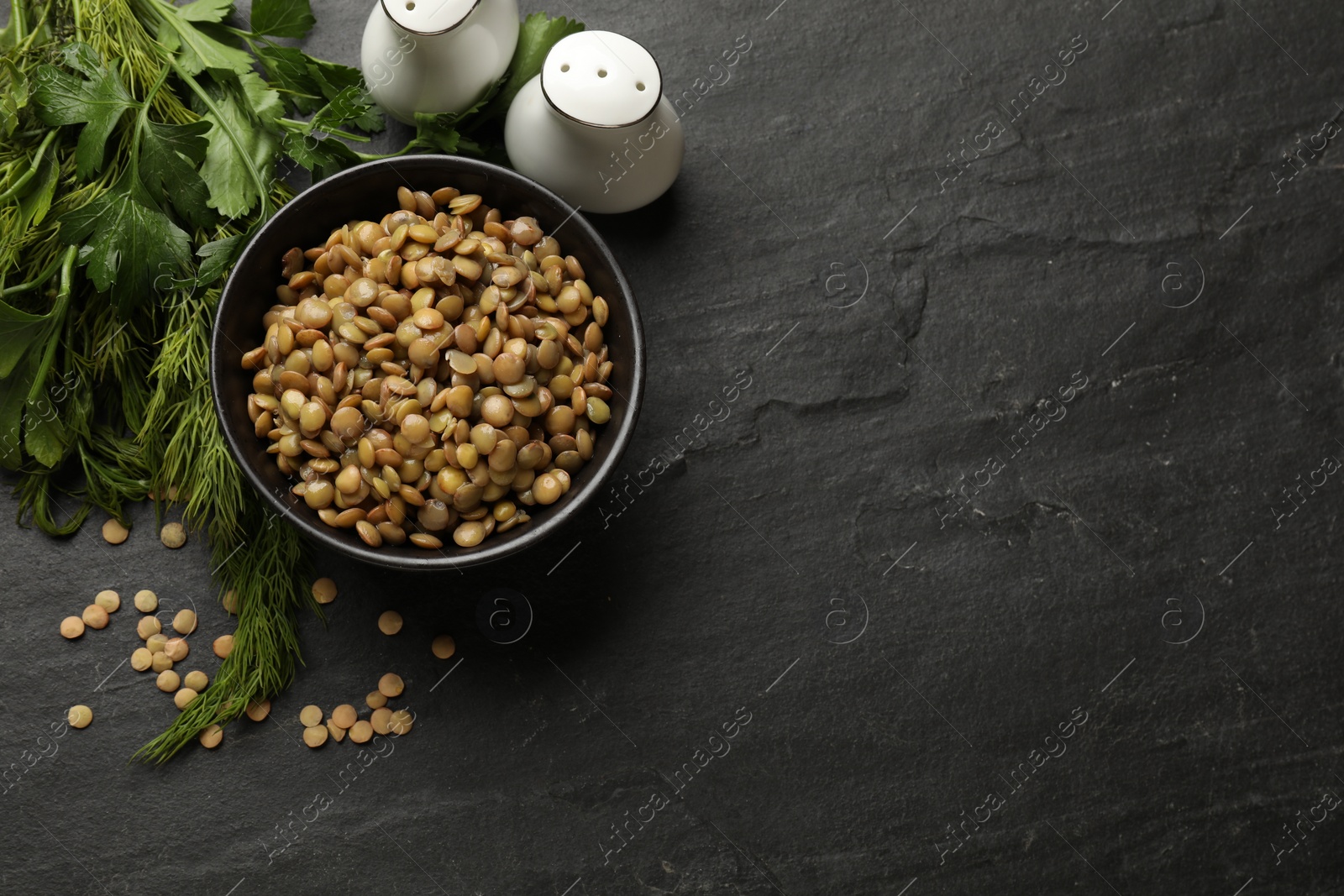 Photo of Delicious lentils in bowl with parsley and dill on grey textured table, flat lay. Space for text