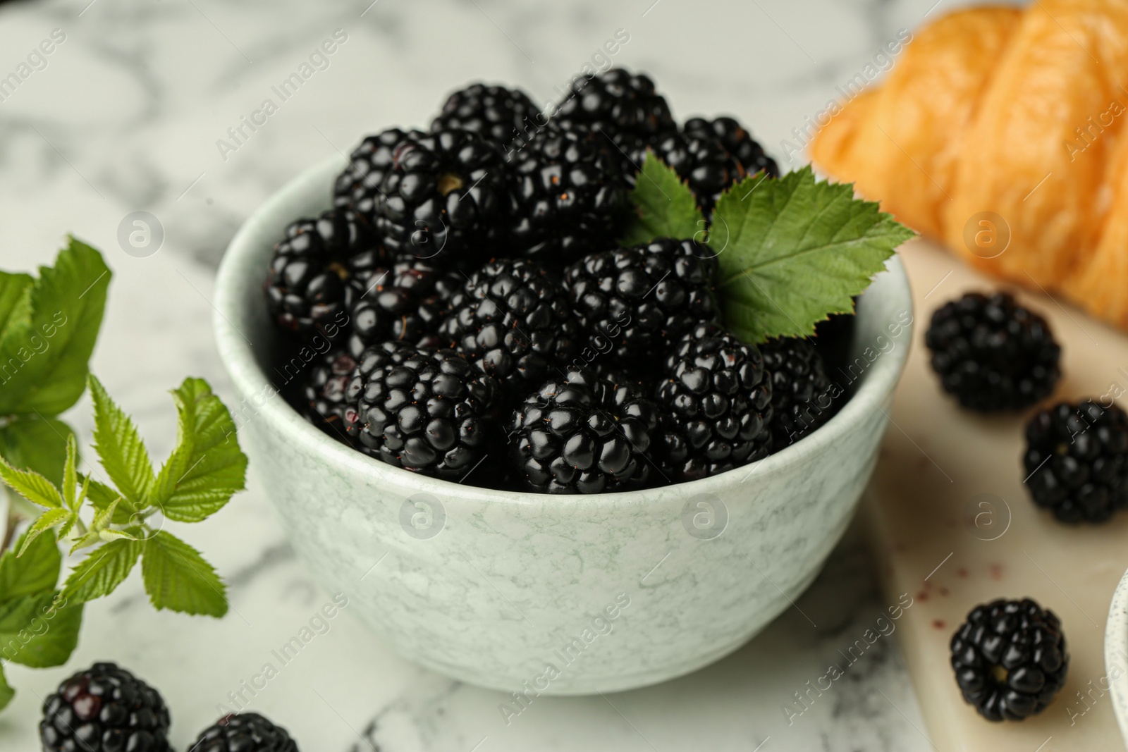 Photo of Bowl of fresh ripe blackberries on white marble table, closeup