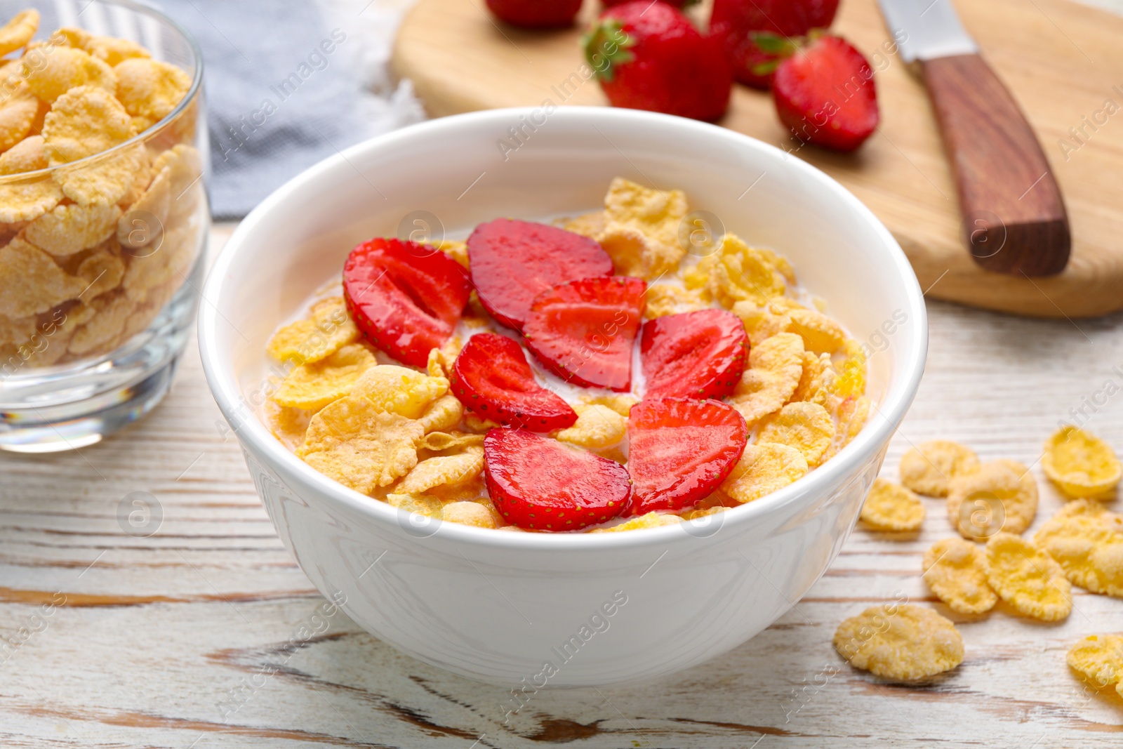 Photo of Bowl of tasty crispy corn flakes with milk and strawberries on white wooden table