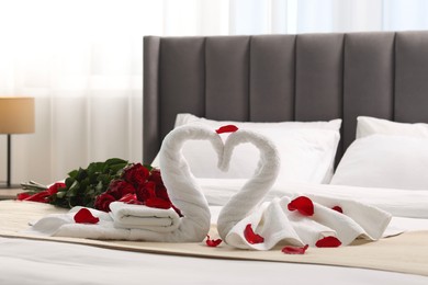 Honeymoon. Swans made of towels and beautiful red roses on bed in room