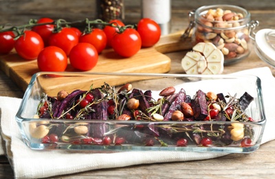 Photo of Baked black carrot with pomegranate seeds and nuts on wooden table