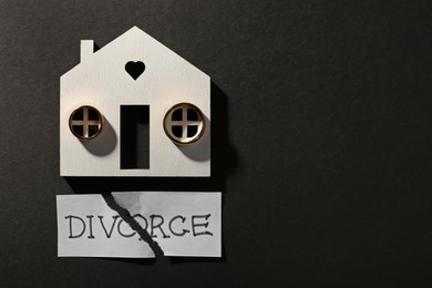 Photo of Pieces of torn card with word Divorce, wooden house and wedding rings on black background, flat lay. Space for text