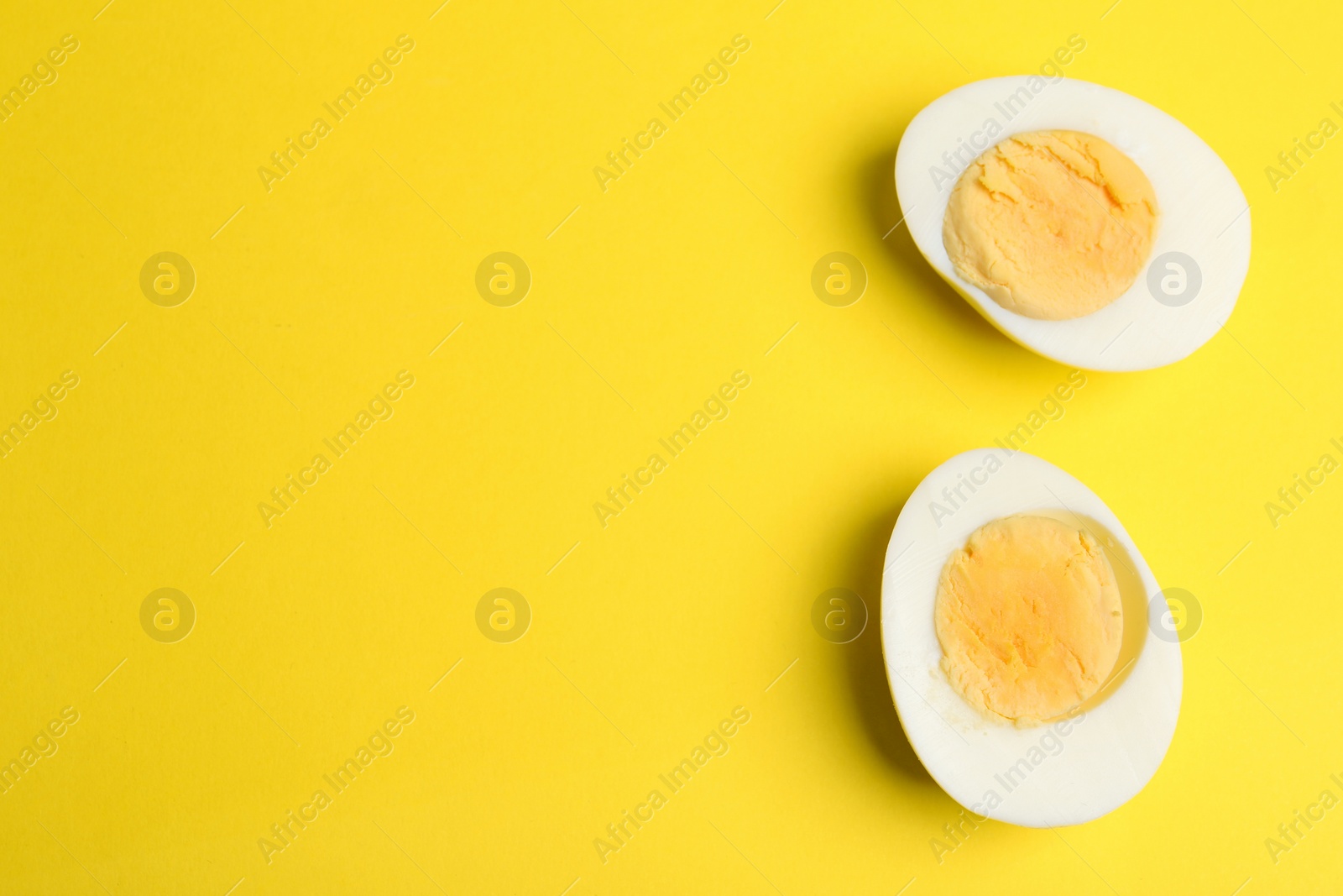 Photo of Halves of fresh hard boiled chicken egg on yellow background, flat lay. Space for text