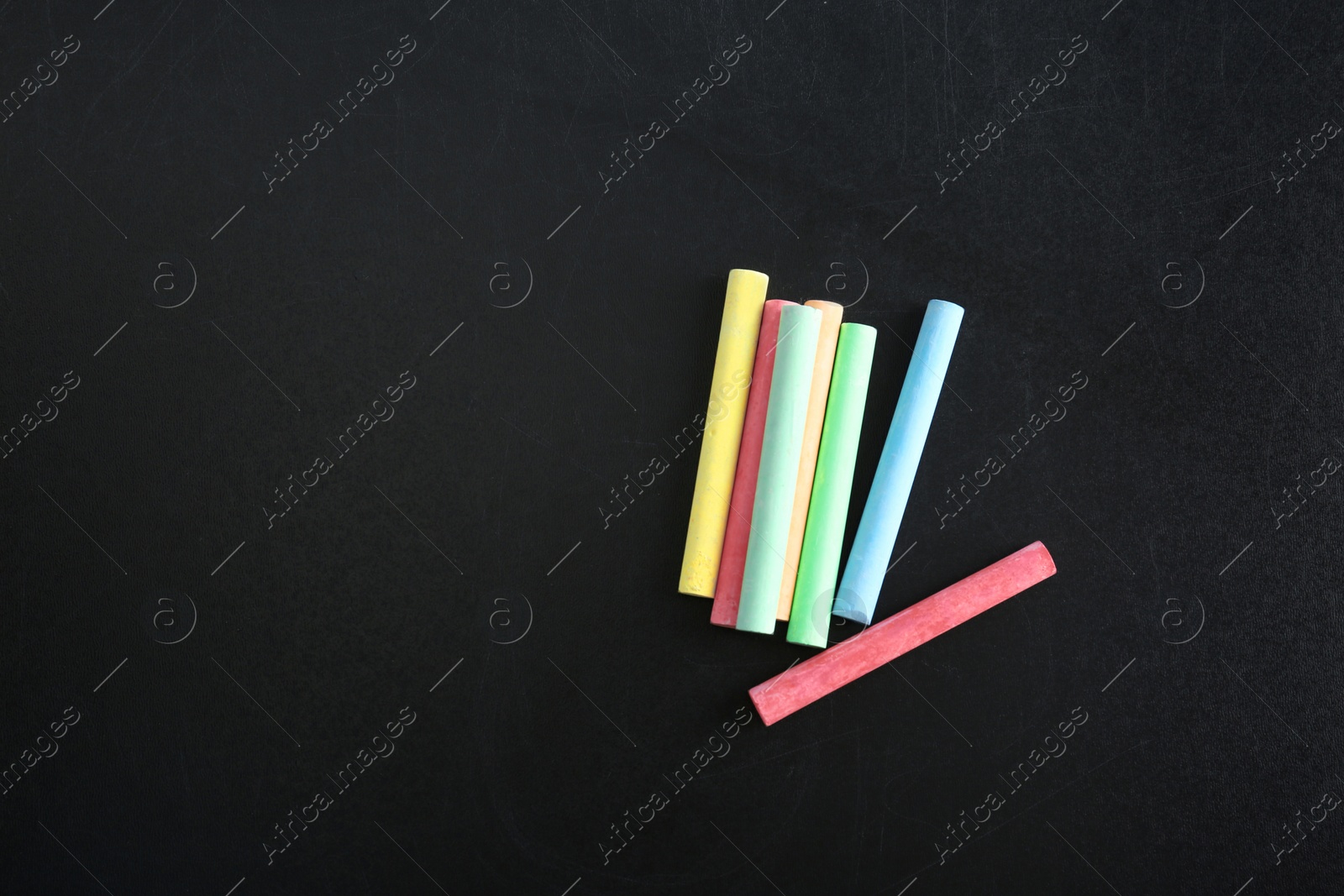 Photo of Color pieces of chalk on blackboard, top view