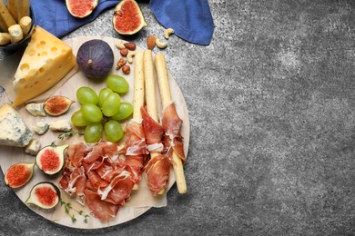 Board with delicious figs, cheese, grapes and bread with proscuitto on grey table, flat lay. Space for text