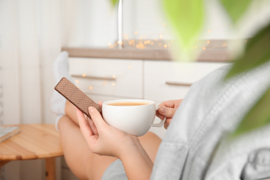 Woman having delicious wafer and coffee for breakfast indoors, closeup