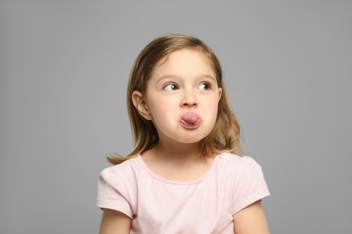 Photo of Funny little girl showing her tongue on grey background
