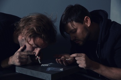 Young addicted men taking drugs on grey background