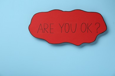 Red card with phrase Are You Ok? on light blue background. Space for text