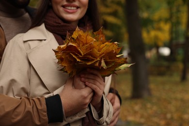 Happy young couple with dry leaves in autumn park, closeup. Space for text