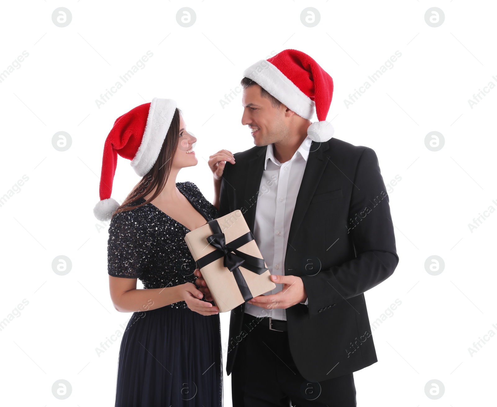 Photo of Beautiful happy couple in Santa hats holding Christmas gift on white background