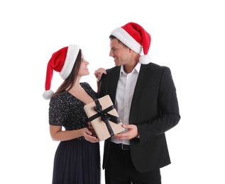 Beautiful happy couple in Santa hats holding Christmas gift on white background