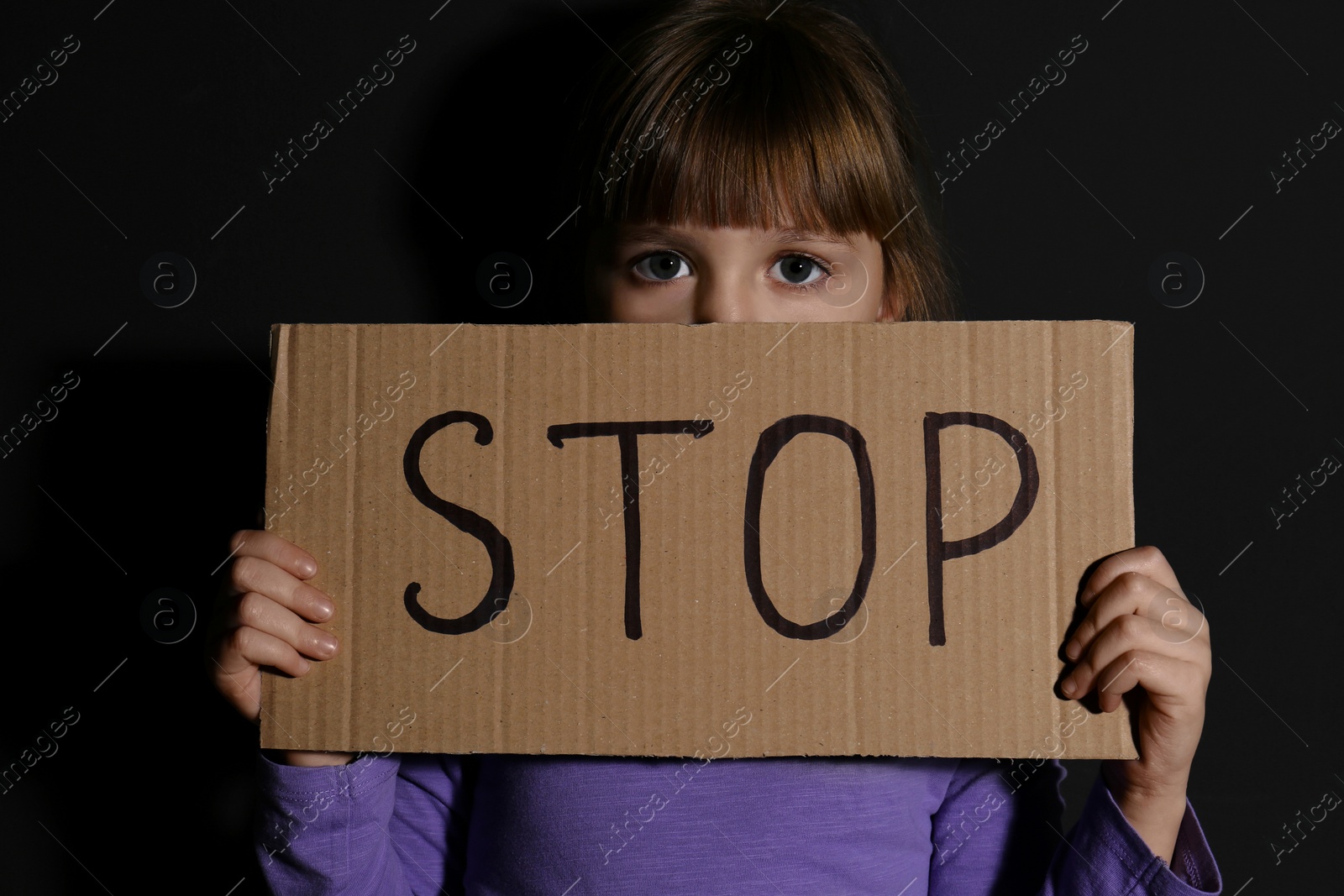 Photo of Abused little girl with sign STOP near black wall. Domestic violence concept