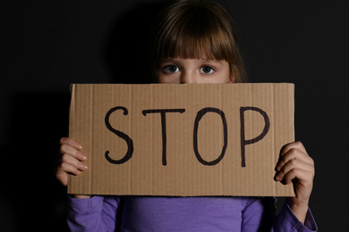 Photo of Abused little girl with sign STOP near black wall. Domestic violence concept