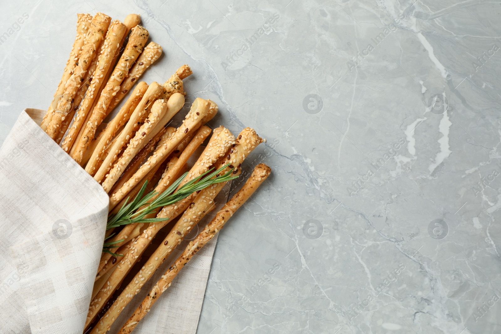 Photo of Delicious grissini sticks and rosemary on grey marble table, flat lay. Space for text