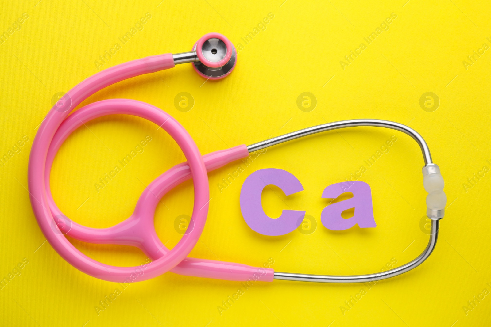 Photo of Stethoscope and calcium symbol made of purple letters on yellow background, flat lay