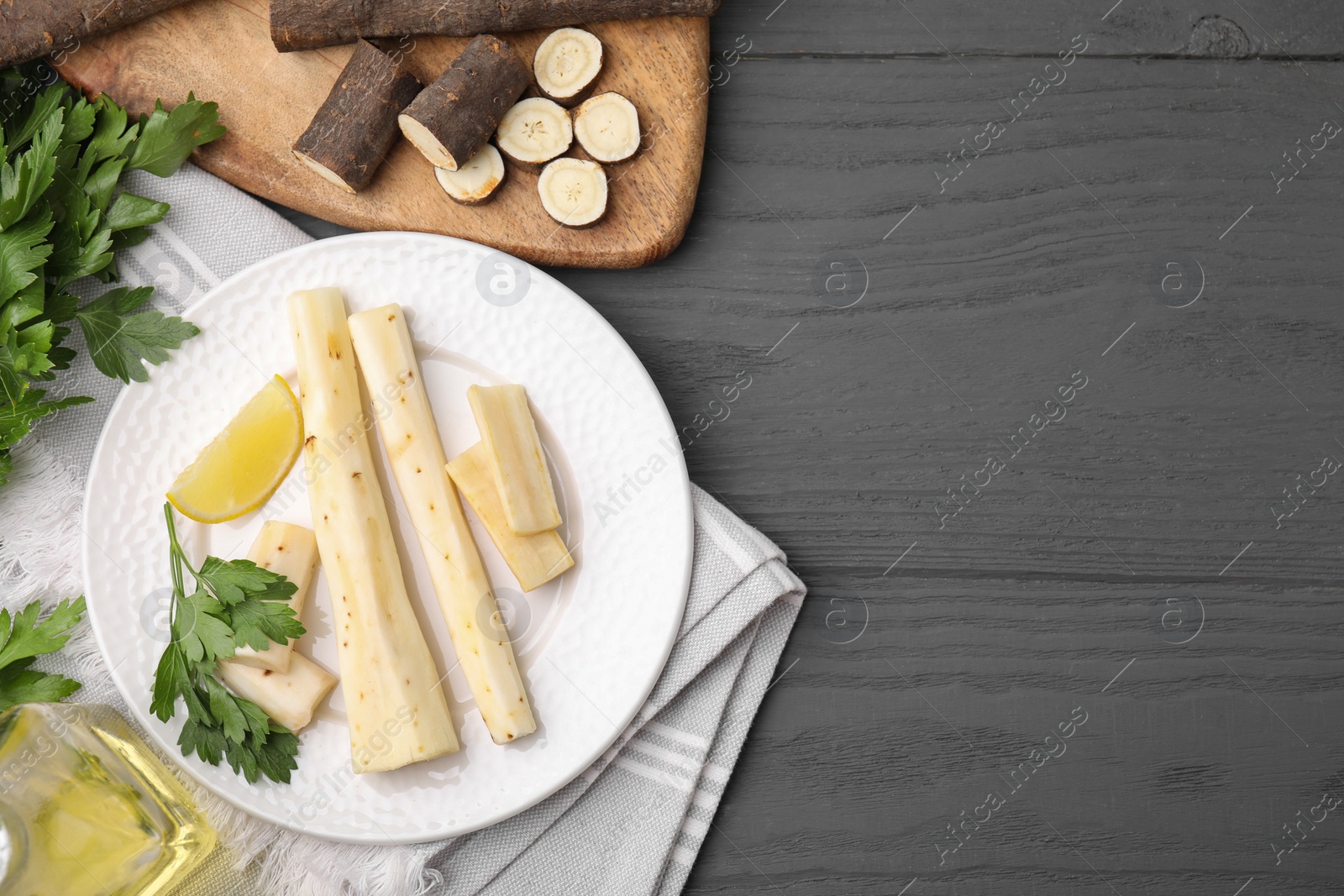 Photo of Cut raw salsify roots with parsley and lemon on grey wooden table, flat lay. Space for text