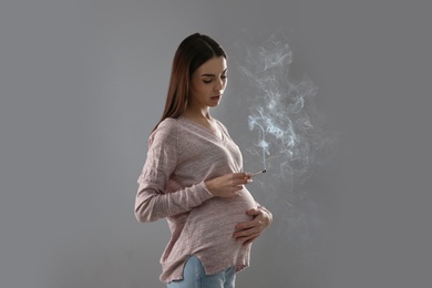 Photo of Young pregnant woman smoking cigarette on grey background