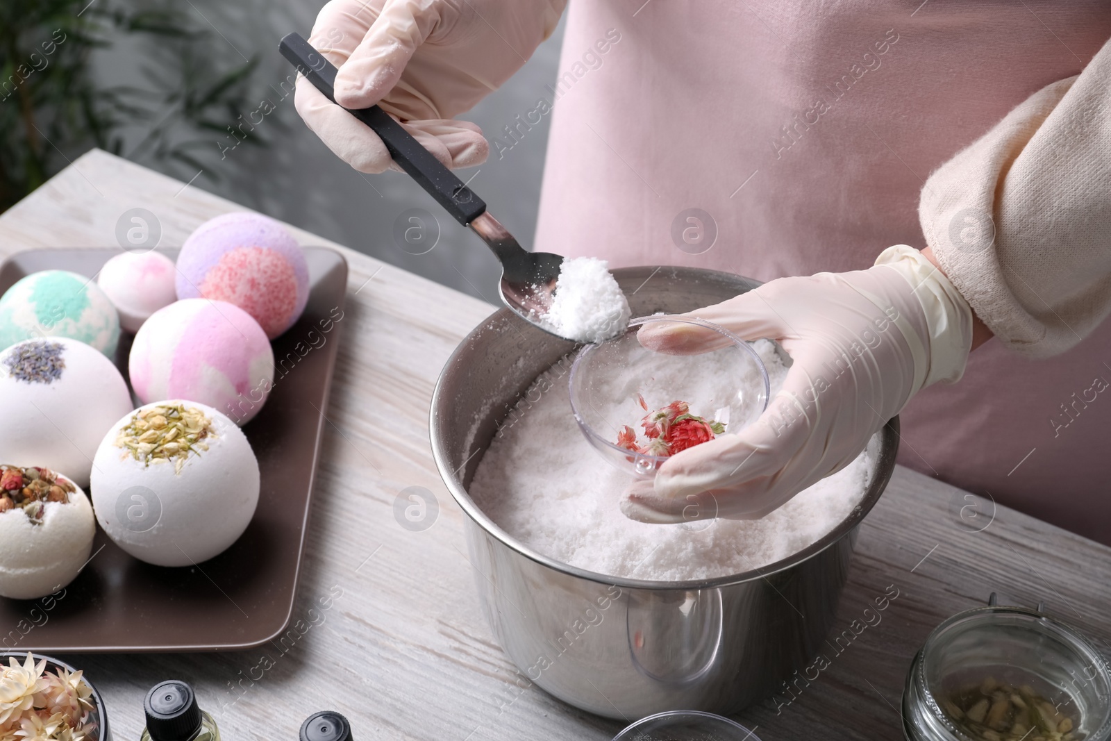 Photo of Woman in gloves making bath bomb at wooden table indoors, closeup