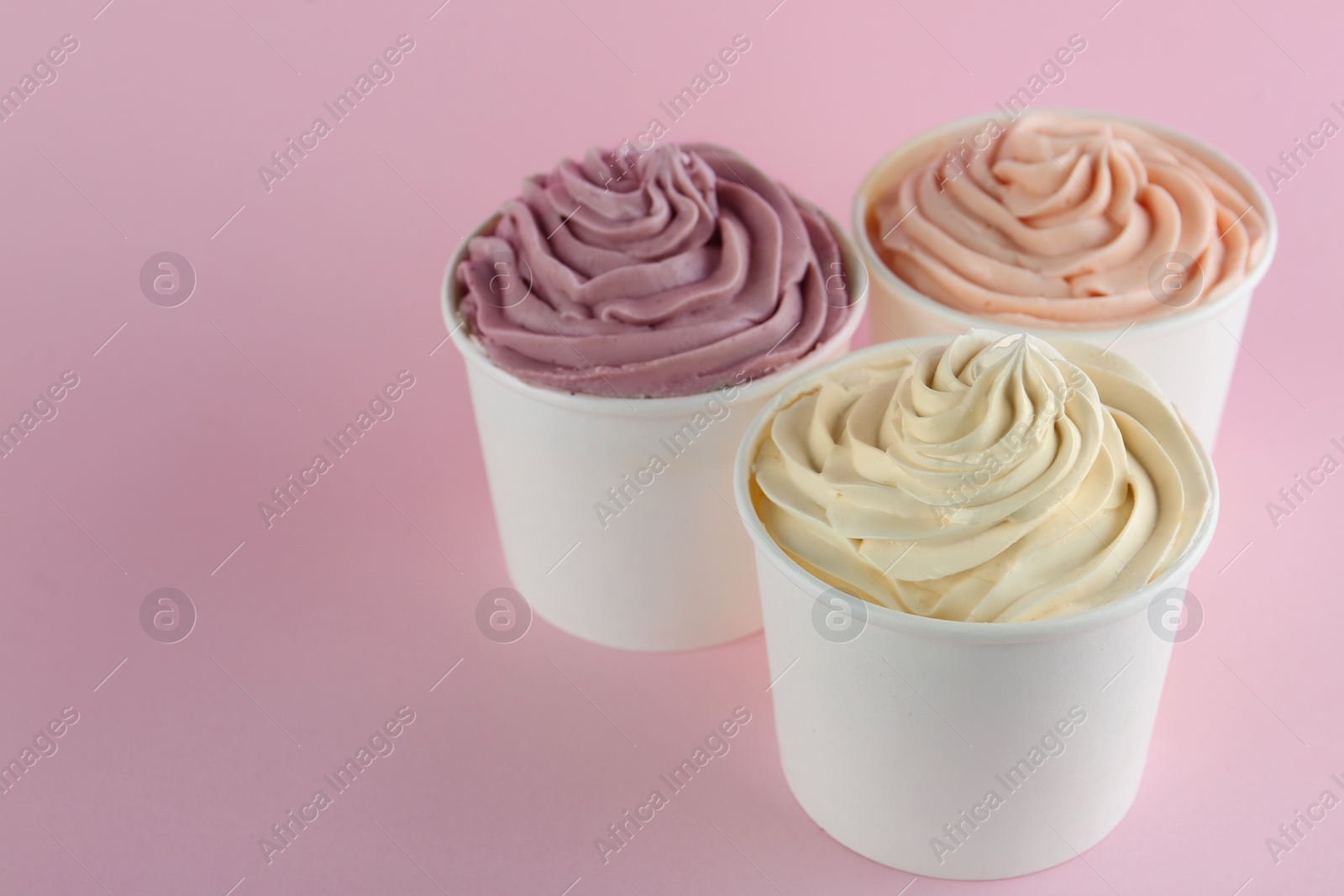 Photo of Cups with tasty frozen yogurts on pink background