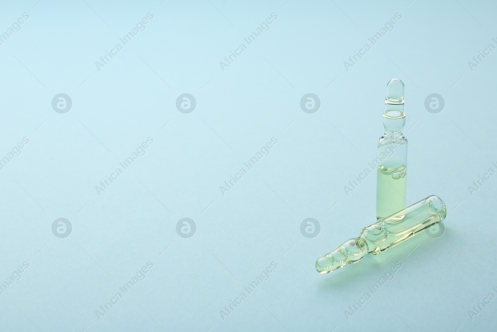 Photo of Glass ampoules with liquid on light blue background. Space for text