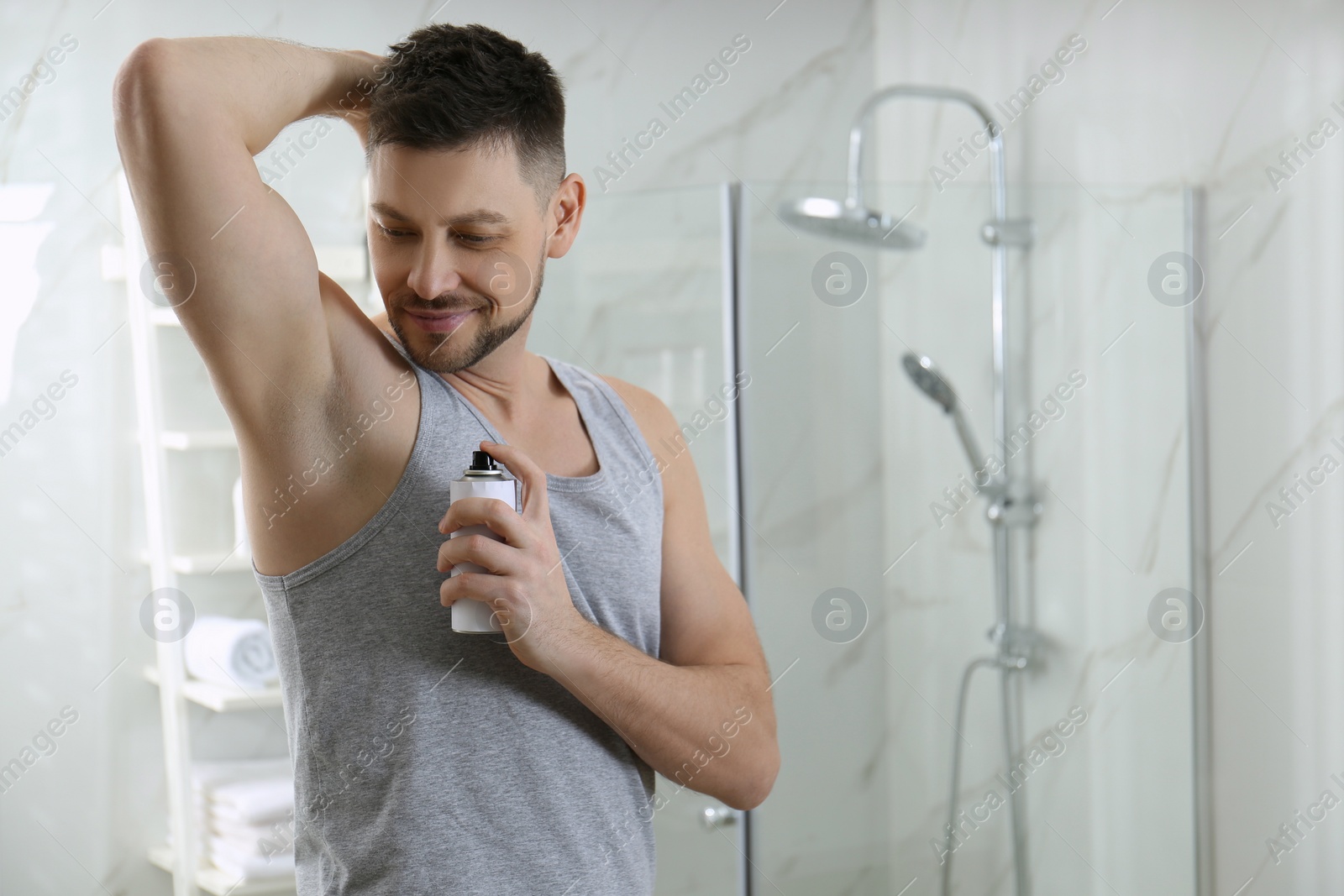 Photo of Handsome man applying deodorant in bathroom. Space for text