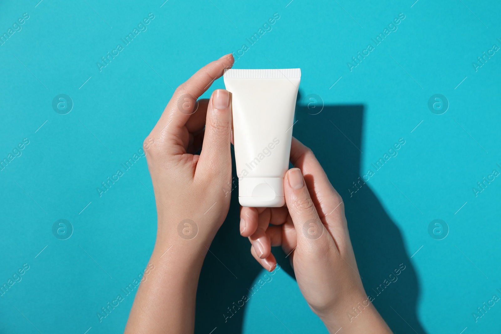 Photo of Woman with tube of hand cream on light blue background, top view