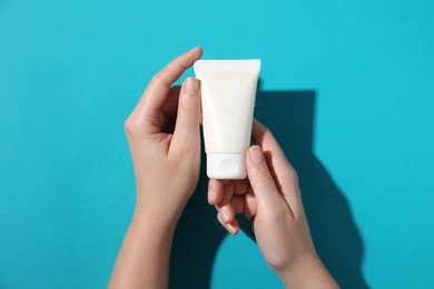 Woman with tube of hand cream on light blue background, top view