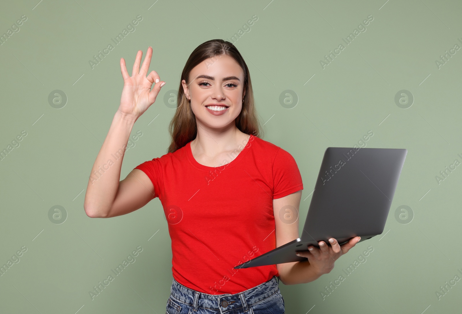 Photo of Happy woman with laptop showing okay gesture on pale green background