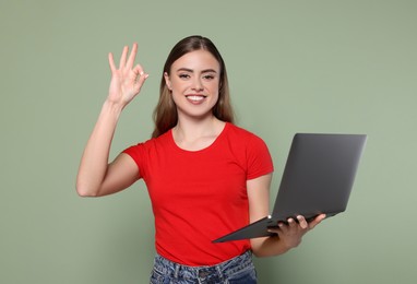 Happy woman with laptop showing okay gesture on pale green background