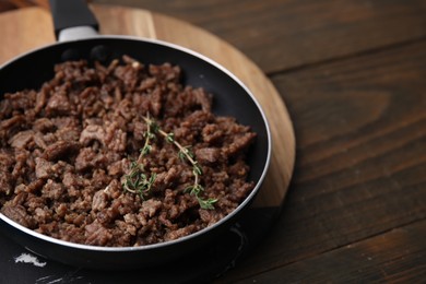 Photo of Fried ground meat and thyme in frying pan on wooden table, closeup. Space for text