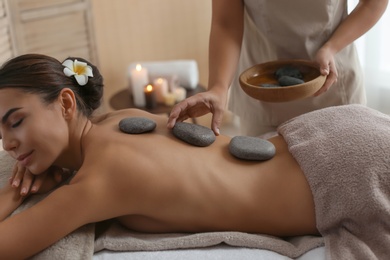 Beautiful young woman getting hot stone massage in spa salon