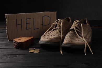 Photo of Poverty. Cardboard sign with word Help, old shoes, piece of bread and coins on black wooden table