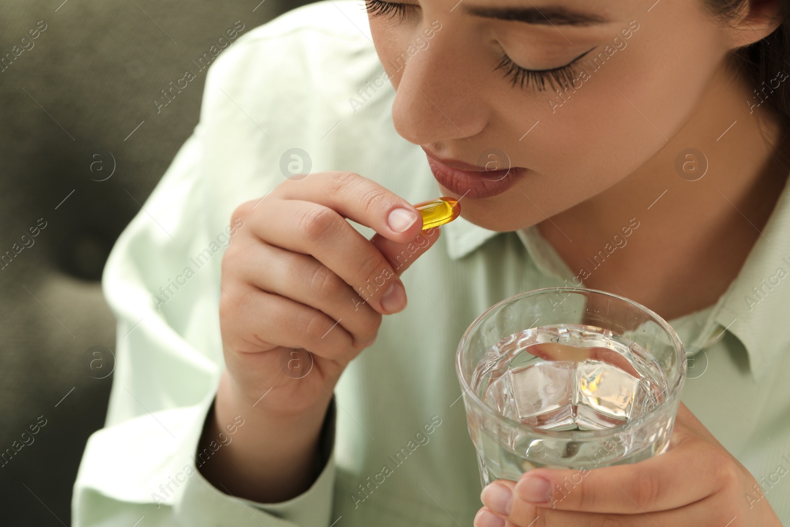 Photo of Young woman with glass of water taking dietary supplement pill, closeup
