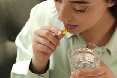 Young woman with glass of water taking dietary supplement pill, closeup