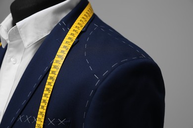 Semi-ready jacket with tailor's measuring tape on mannequin against grey background, closeup