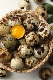 Photo of Wicker bowl with whole and cracked quail eggs on white table, flat lay