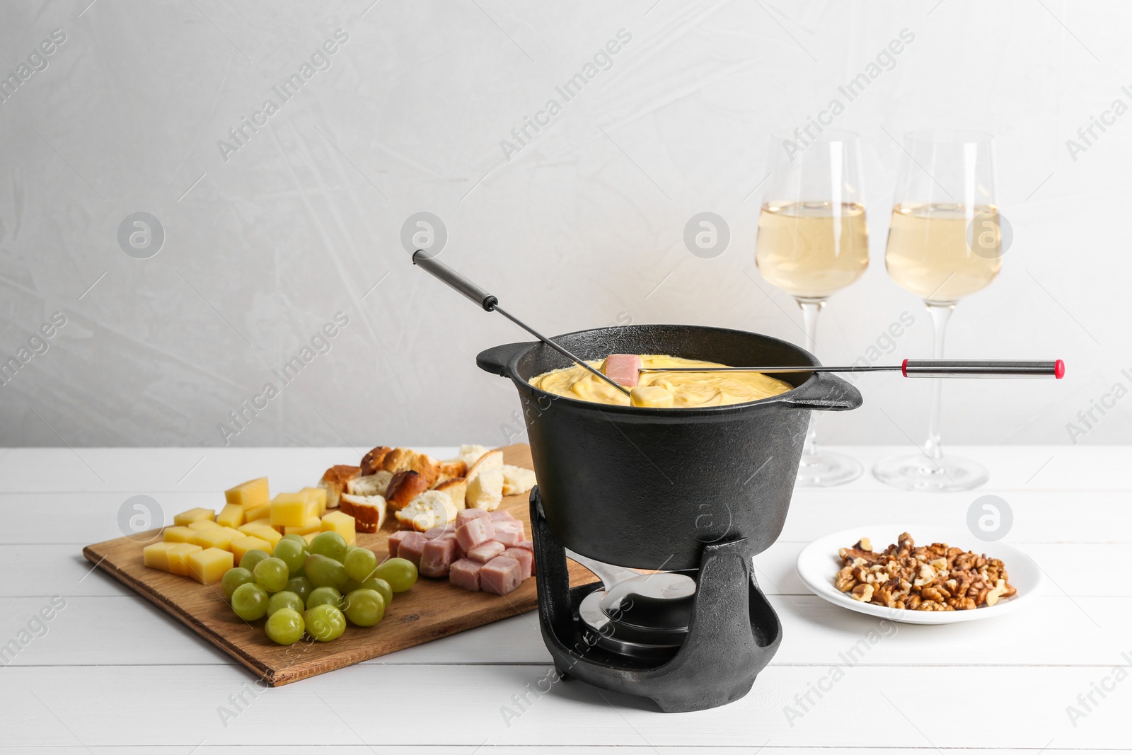 Photo of Fondue pot with tasty melted cheese, forks, wine and different snacks on white wooden table