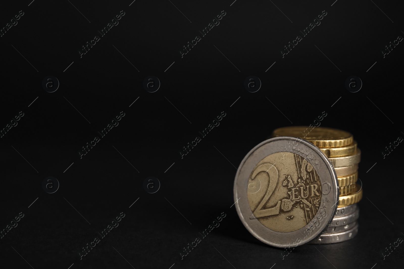 Photo of Many Euro coins stacked on black background, closeup. Space for text