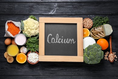 Photo of Set of natural food and chalkboard with written word Calcium on black wooden table, flat lay