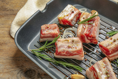 Photo of Grill pan with raw ribs and seasonings on wooden table, closeup
