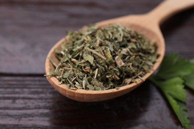 Photo of Spoon of dried aromatic parsley and fresh leaves on wooden table, closeup