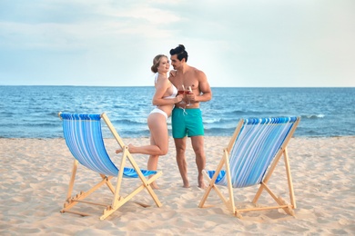 Photo of Happy young couple near deck chairs at sea beach